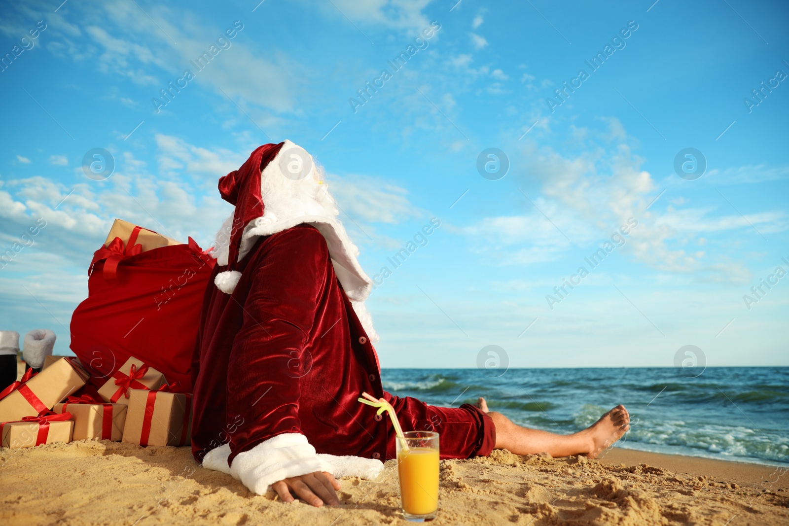 Photo of Santa Claus with cocktail and bag of presents relaxing on beach. Christmas vacation