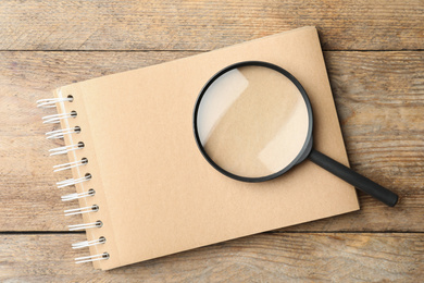 Photo of Top view of magnifier glass and empty notebook on wooden background, space for text. Find keywords concept