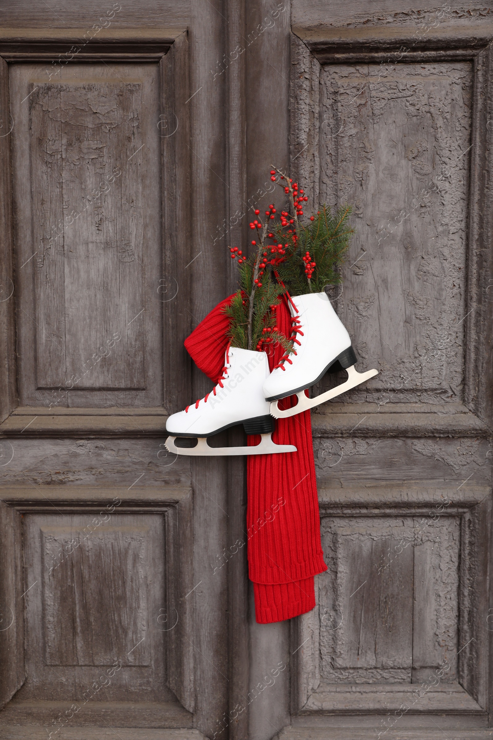 Photo of Pair of ice skates with Christmas decor hanging on old wooden door