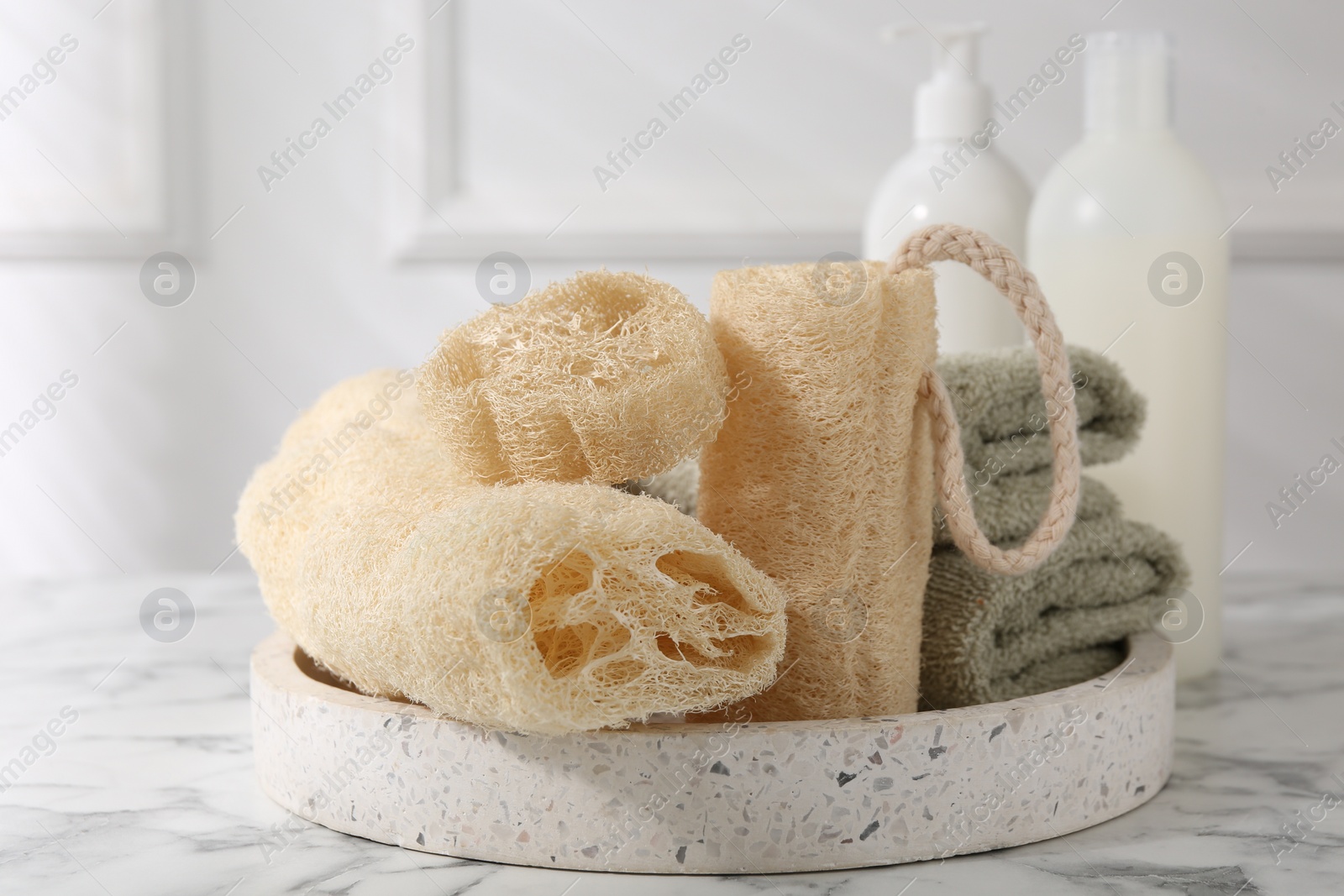 Photo of Loofah sponges, towels, soap and cosmetic products on white marble table