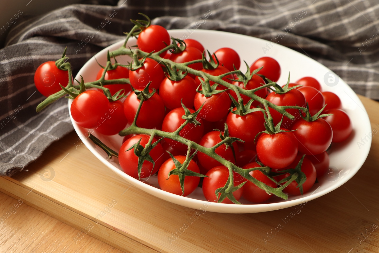 Photo of Plate of ripe whole cherry tomatoes on wooden table, closeup