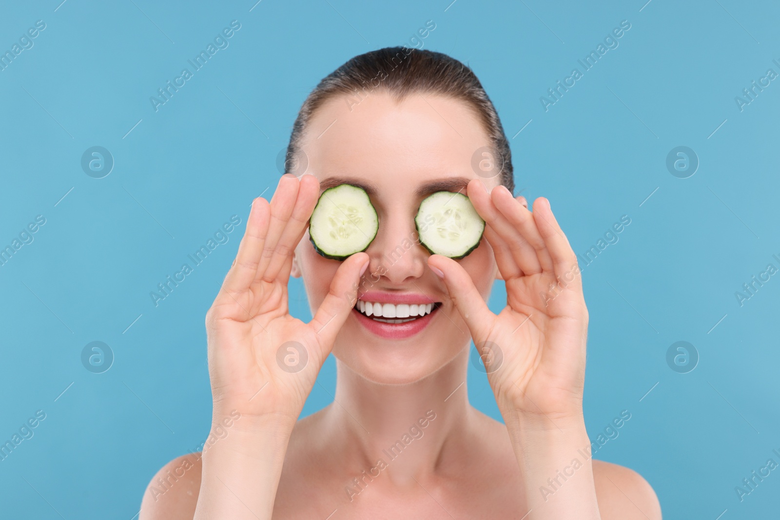 Photo of Beautiful woman covering eyes with pieces of cucumber on light blue background