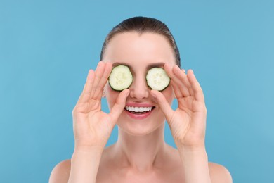 Photo of Beautiful woman covering eyes with pieces of cucumber on light blue background