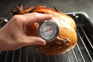 Photo of Woman measuring temperature of whole roasted turkey with meat thermometer, closeup