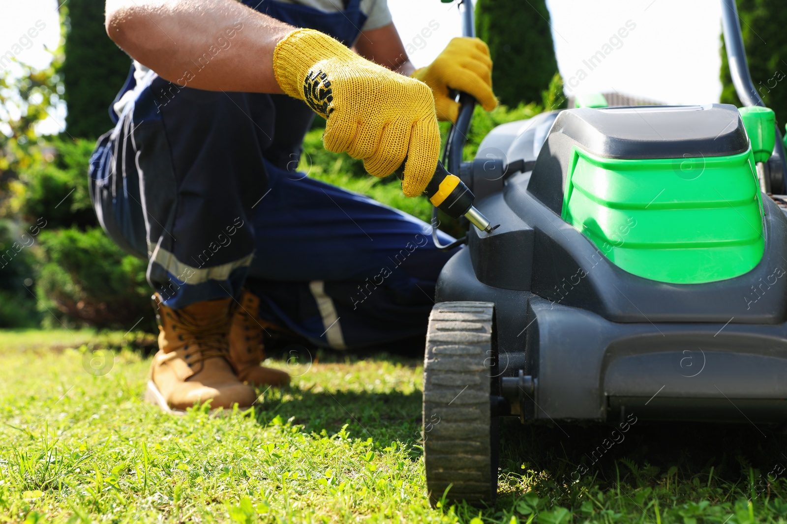 Photo of Young man with screwdriver fixing lawn mower in garden, closeup