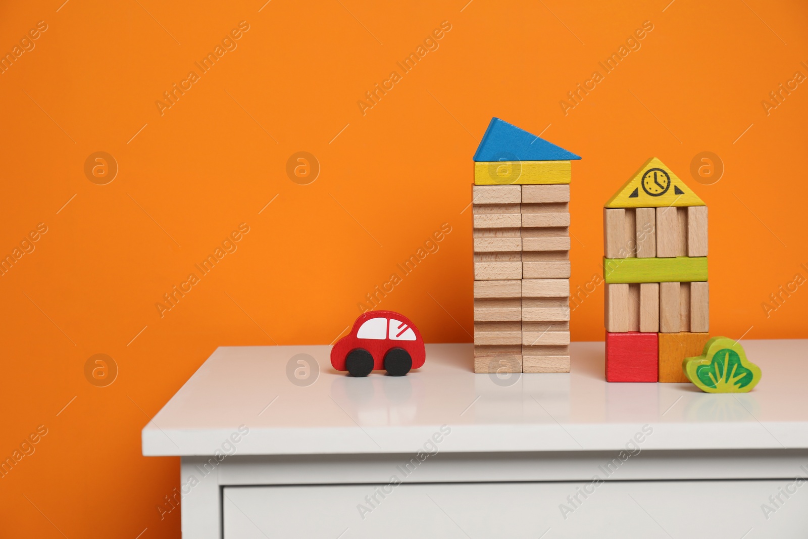 Photo of Set of wooden toys on white chest of drawers near orange wall, space for text. Children's development