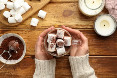 Photo of Woman holding cup of aromatic hot chocolate with marshmallows and cocoa powder at wooden table, top view