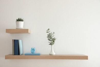 Wooden shelves with beautiful plants, alarm clock and books on light wall