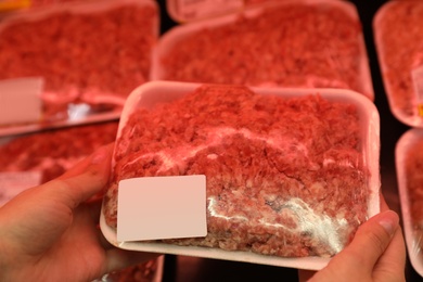 Woman taking packed forcemeat from shelf in supermarket