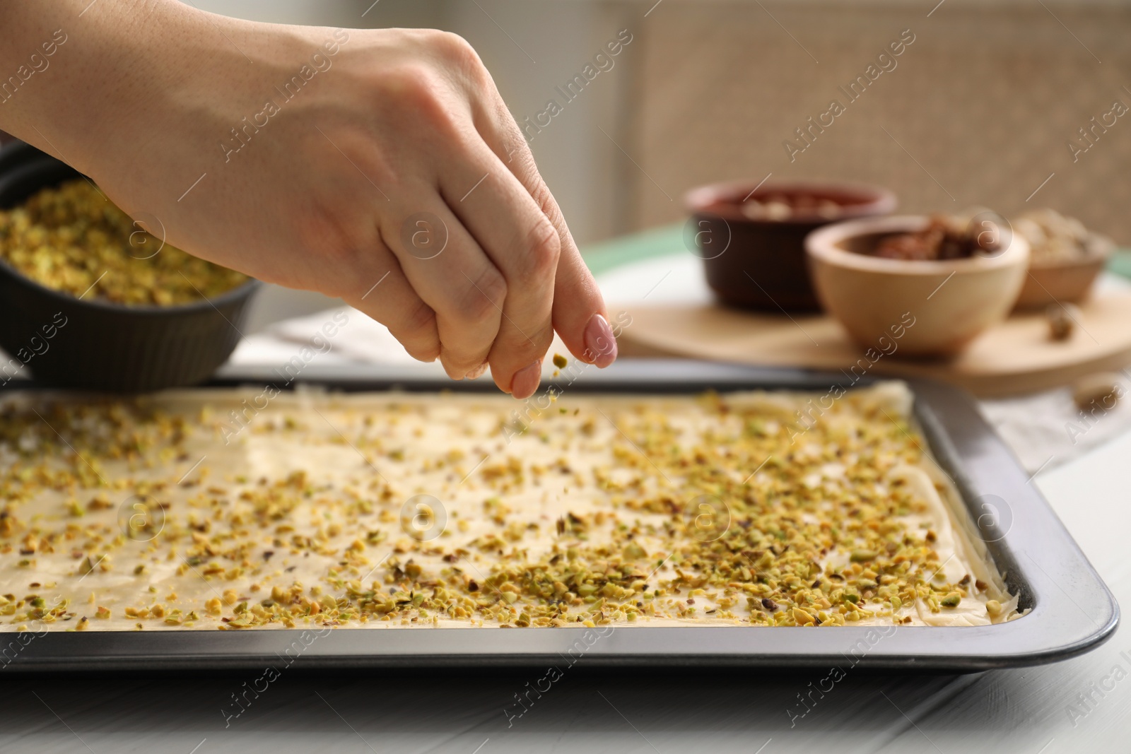 Photo of Making delicious baklava. Woman adding chopped nuts to dough at white wooden table, closeup