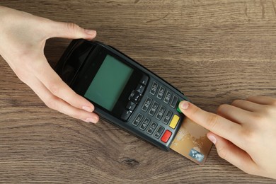 Women with credit card using modern payment terminal at wooden table, top view