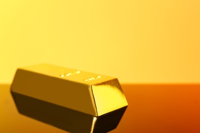 Photo of Precious shiny gold bar on mirror surface, space for text