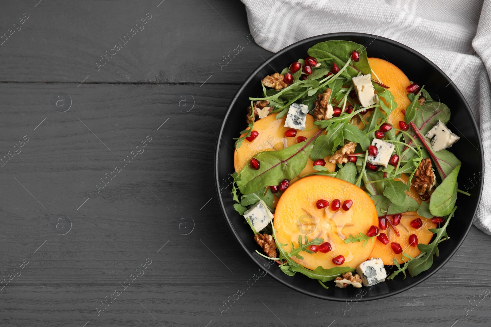 Photo of Tasty salad with persimmon, blue cheese, pomegranate and walnuts served on grey wooden table, top view. Space for text