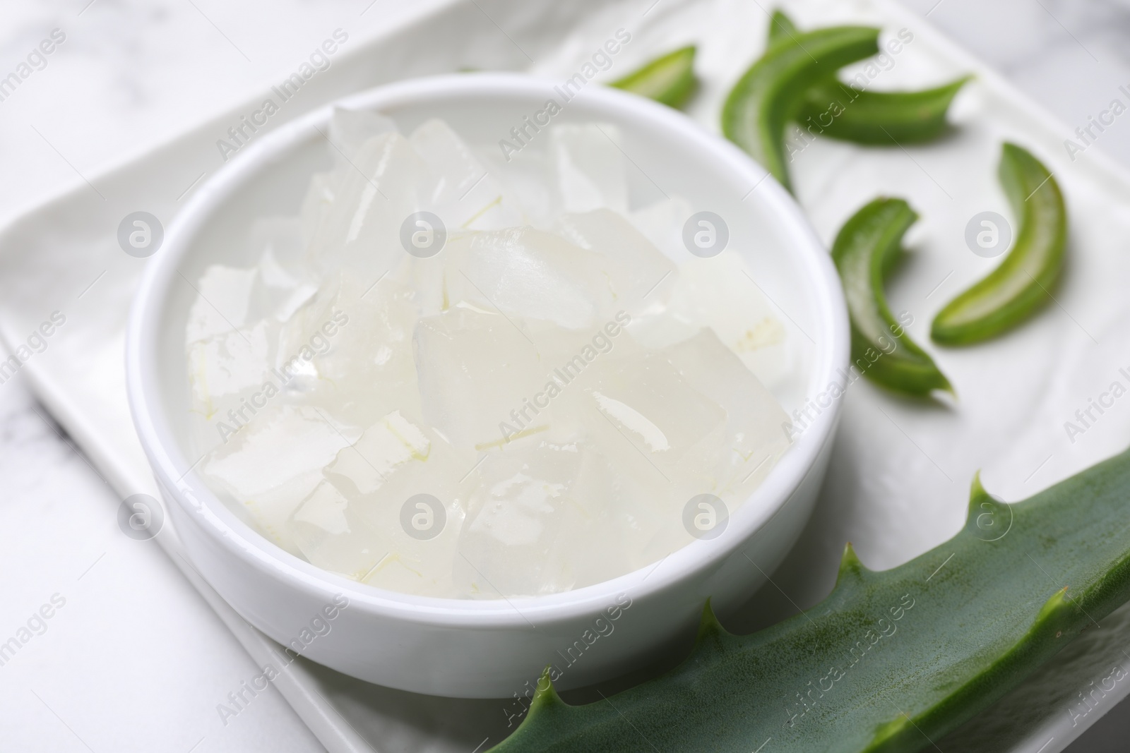 Photo of Aloe vera gel and slices of plant on white table, closeup