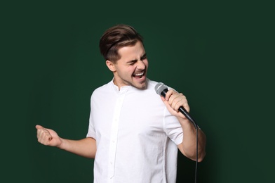 Photo of Young handsome man in casual clothes singing with microphone on color background. Space for text