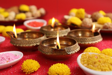 Photo of Diwali celebration. Diya lamps, rangoli and chrysanthemum flowers on shiny red table, closeup