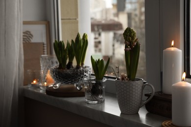 Photo of Beautiful bulbous plants and burning candles on windowsill indoors. Spring time
