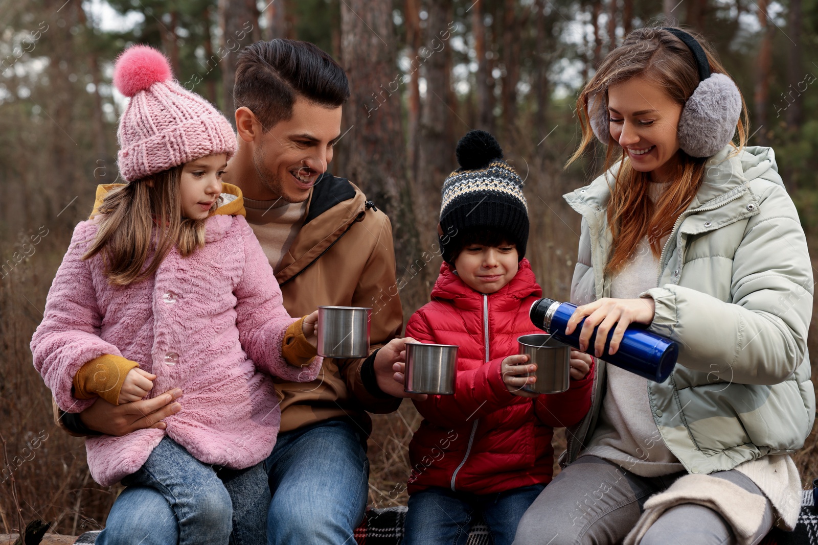 Photo of Happy family with cups of hot tea spending time together in forest
