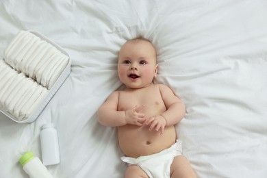 Photo of Cute baby, diapers and cosmetic products on white bed, top view