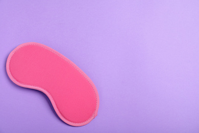 Photo of Pink sleeping mask on violet background, top view with space for text. Bedtime accessory