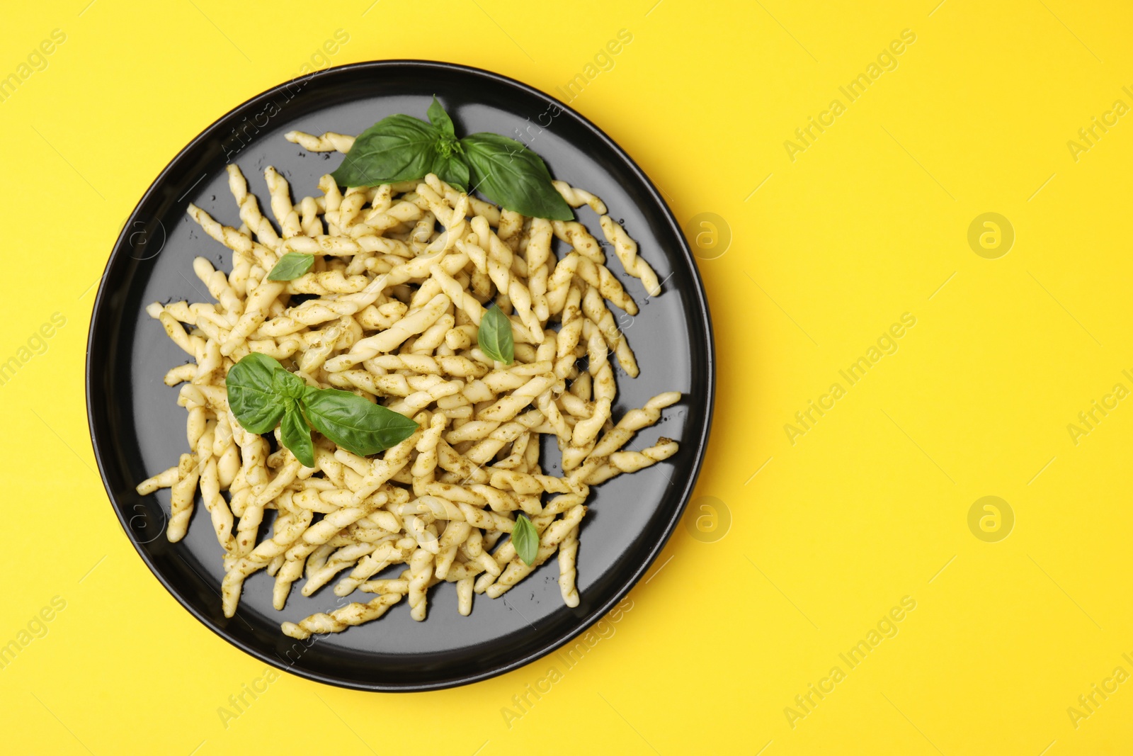 Photo of Plate of delicious trofie pasta with pesto sauce and basil leaves on yellow background, top view. Space for text