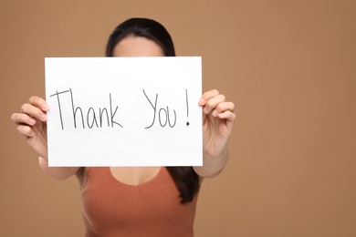 Photo of Woman holding card with phrase Thank You on brown background, selective focus. Space for text