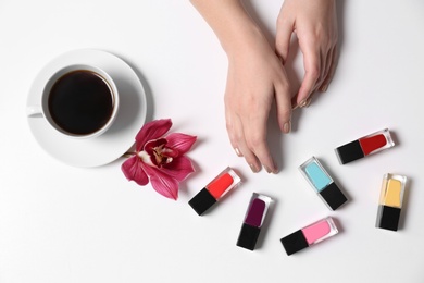 Woman with gold manicure holding hands near nail polishes and cup of coffee on white background, top view