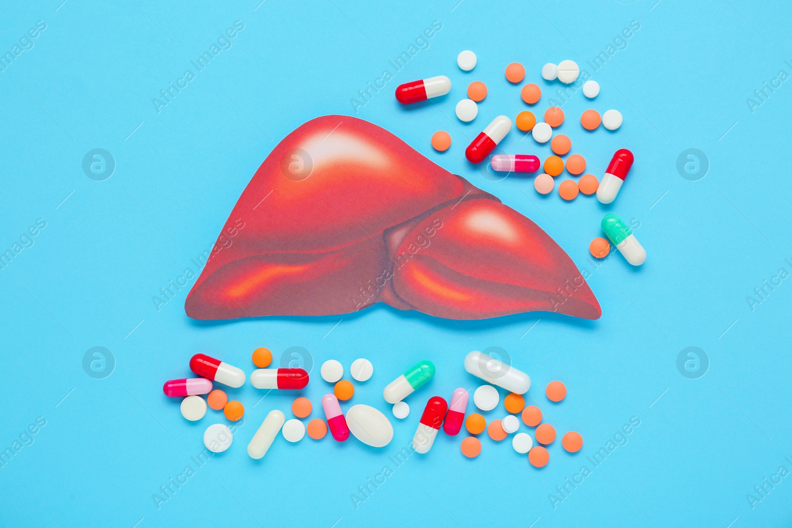 Photo of Paper liver and pills on light blue background, flat lay. Hepatitis treatment