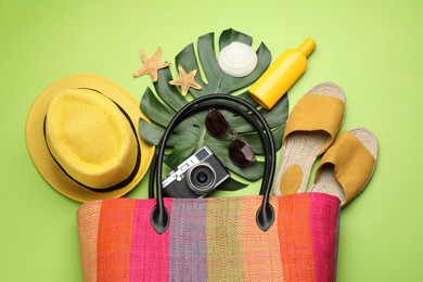 Stylish bag with beach accessories on light green background, flat lay