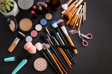 Photo of Flat lay composition with makeup brushes and cosmetic products on black background