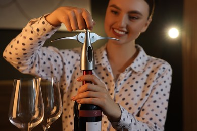 Romantic dinner. Woman opening wine bottle with corkscrew indoors, selective focus
