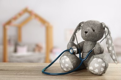 Image of Toy bunny with stethoscope on wooden table indoors, space for text. Pediatrician practice