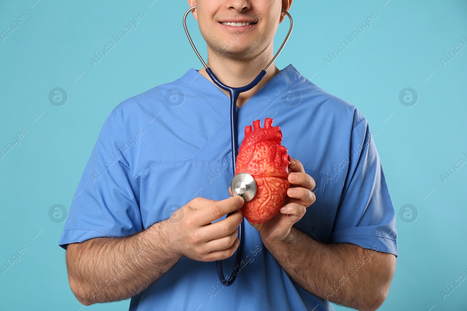 Photo of Doctor with stethoscope and model of heart on light blue background, closeup. Cardiology concept