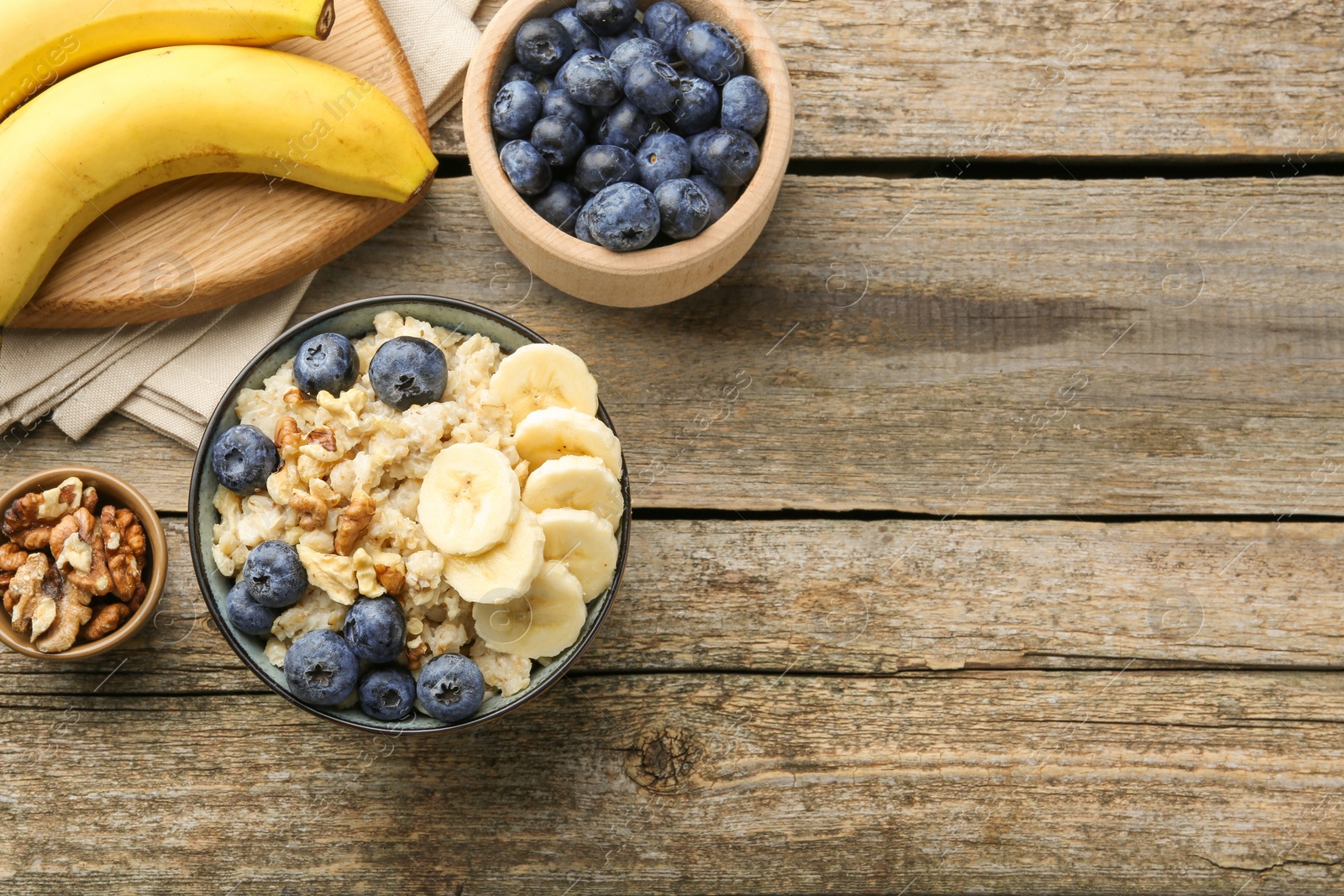 Photo of Tasty oatmeal with banana, blueberries and walnuts served in bowl on wooden table, flat lay. Space for text
