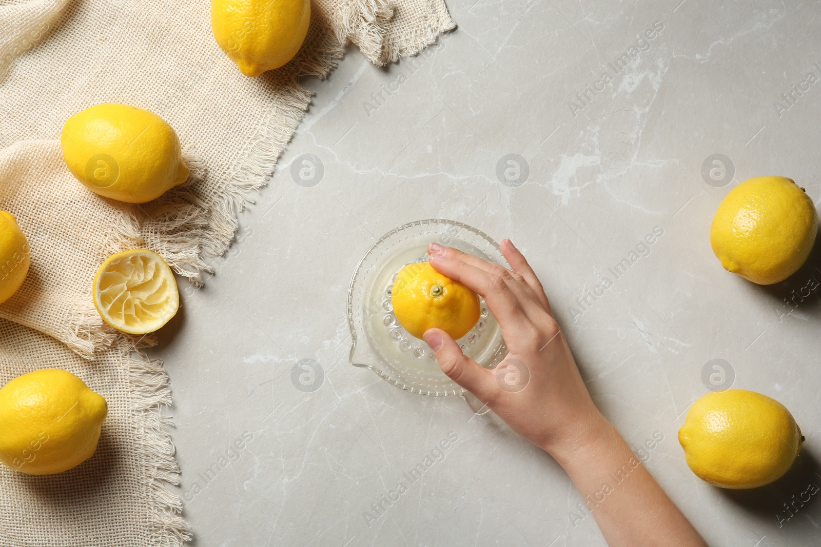 Photo of Young woman squeezing lemon with juicer on light table