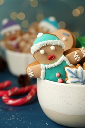 Photo of Delicious homemade Christmas cookies in bowl on blue wooden table against blurred festive lights, closeup