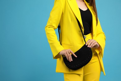 Fashionable woman with stylish bag on light blue background, closeup