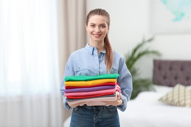 Woman holding folded clean clothes in bedroom. Laundry day