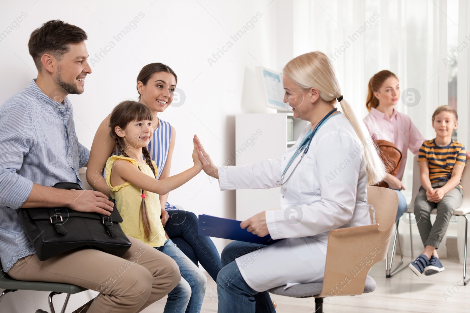 Photo of Cute child sitting with her parents and giving high five to doctor in hospital