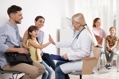 Cute child sitting with her parents and giving high five to doctor in hospital