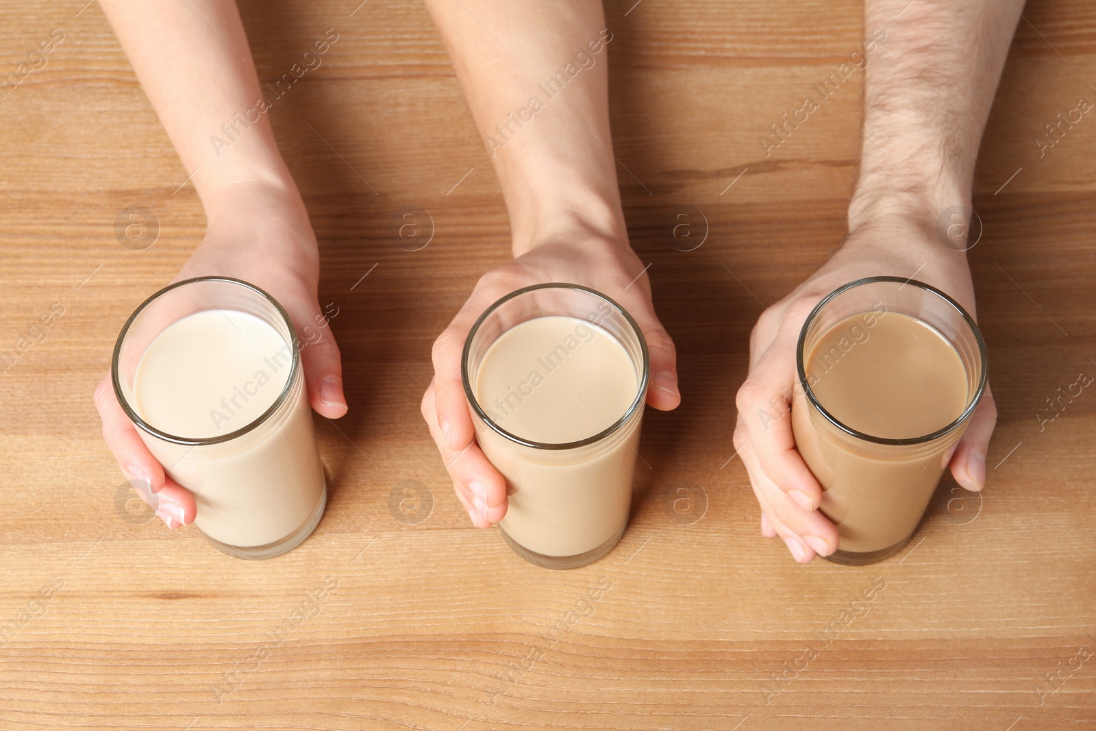 Photo of People holding glasses with protein shakes on wooden background, above view