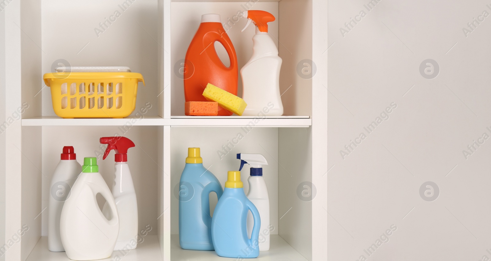 Photo of Shelving unit with different cleaning supplies and tools near white wall