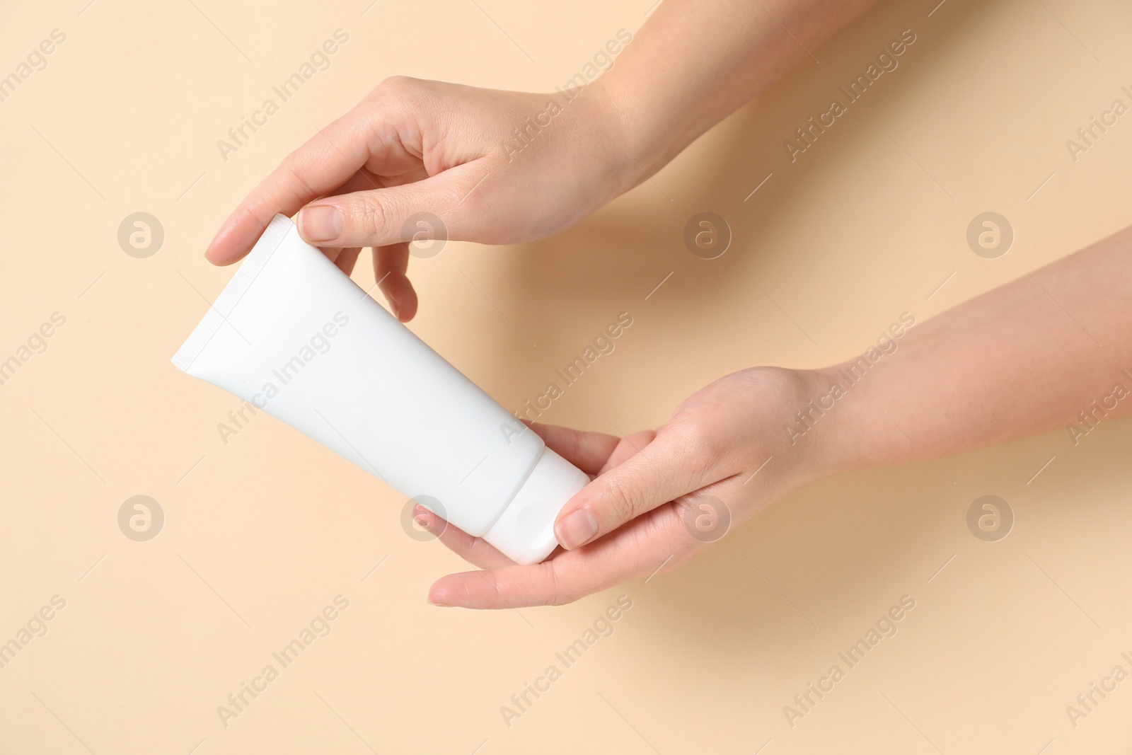 Photo of Woman with tube of hand cream on beige background, closeup