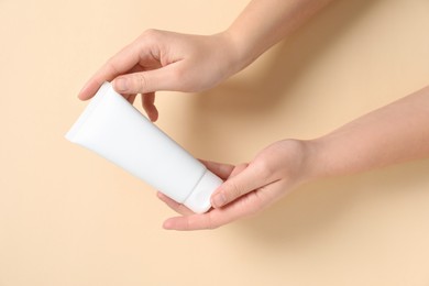 Woman with tube of hand cream on beige background, closeup