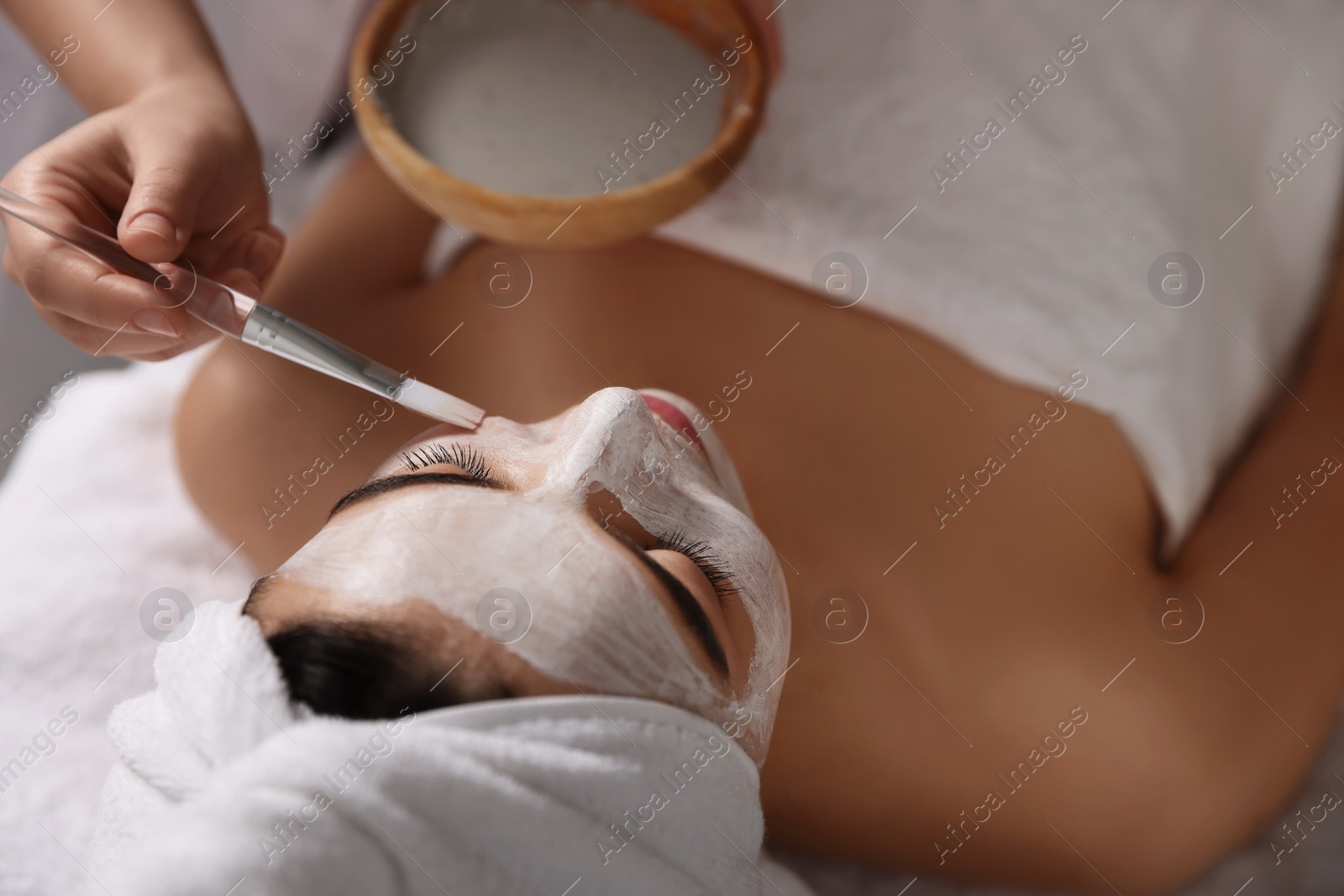 Photo of Cosmetologist applying mask on woman's face in spa salon, closeup