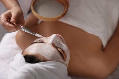 Photo of Cosmetologist applying mask on woman's face in spa salon, closeup