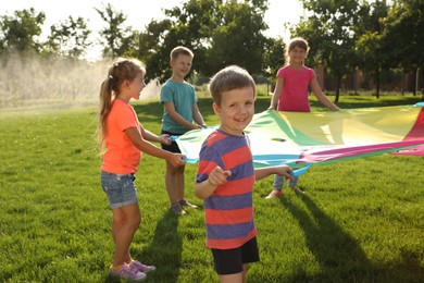 Group of children playing with rainbow playground parachute on green grass. Summer camp activity