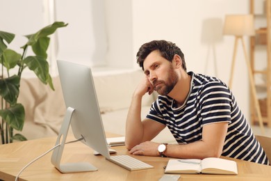 Photo of Home workplace. Tired man working with computer at wooden desk in room