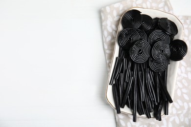 Photo of Tasty black liquorice candies on white wooden table, top view. Space for text