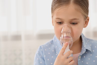 Photo of Sick little girl using nebulizer for inhalation indoors